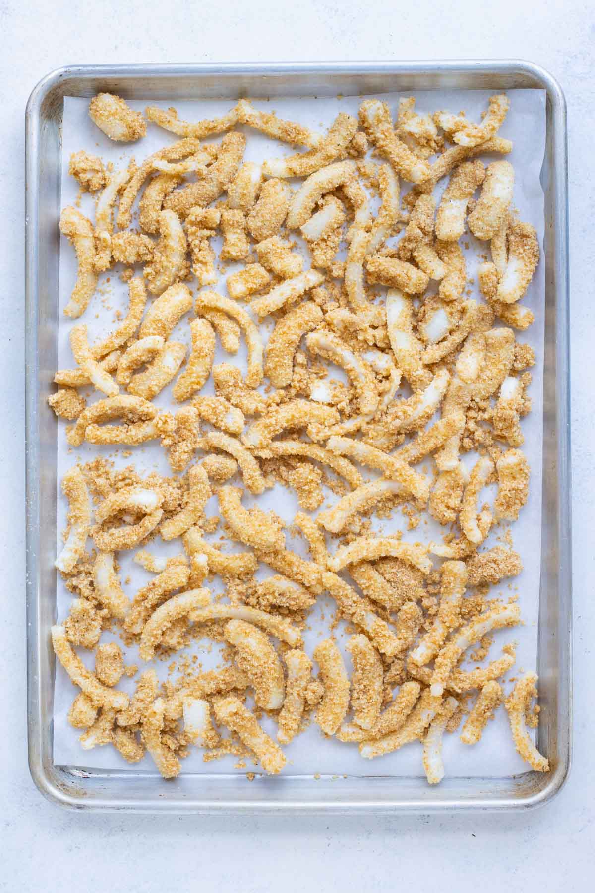 A tray of uncooked fried onions ready to bake for a dairy-free green bean casserole.