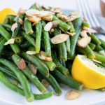 A serving of cooked green beans with lemon zest and toasted almonds on top.