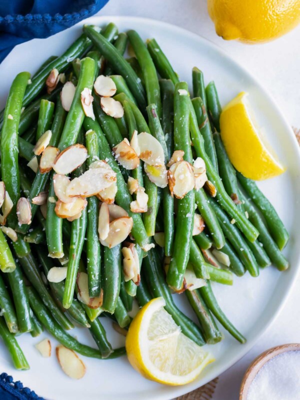 A plate full of green beans almondine with lemon wedges and a fork.