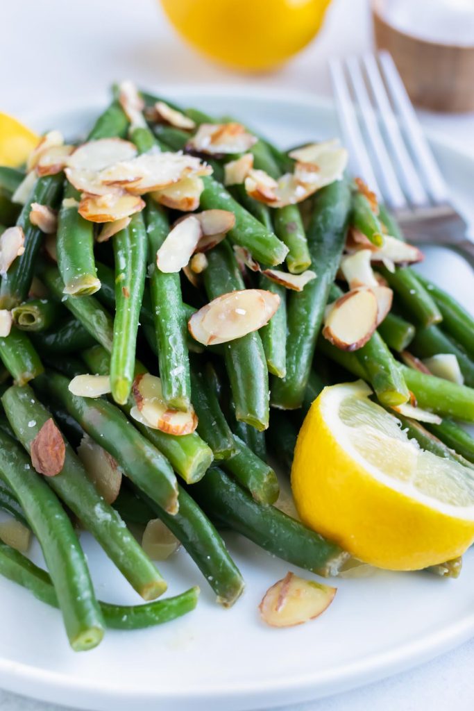 A white plate with a green beans almondine recipe with a fresh lemon slice.