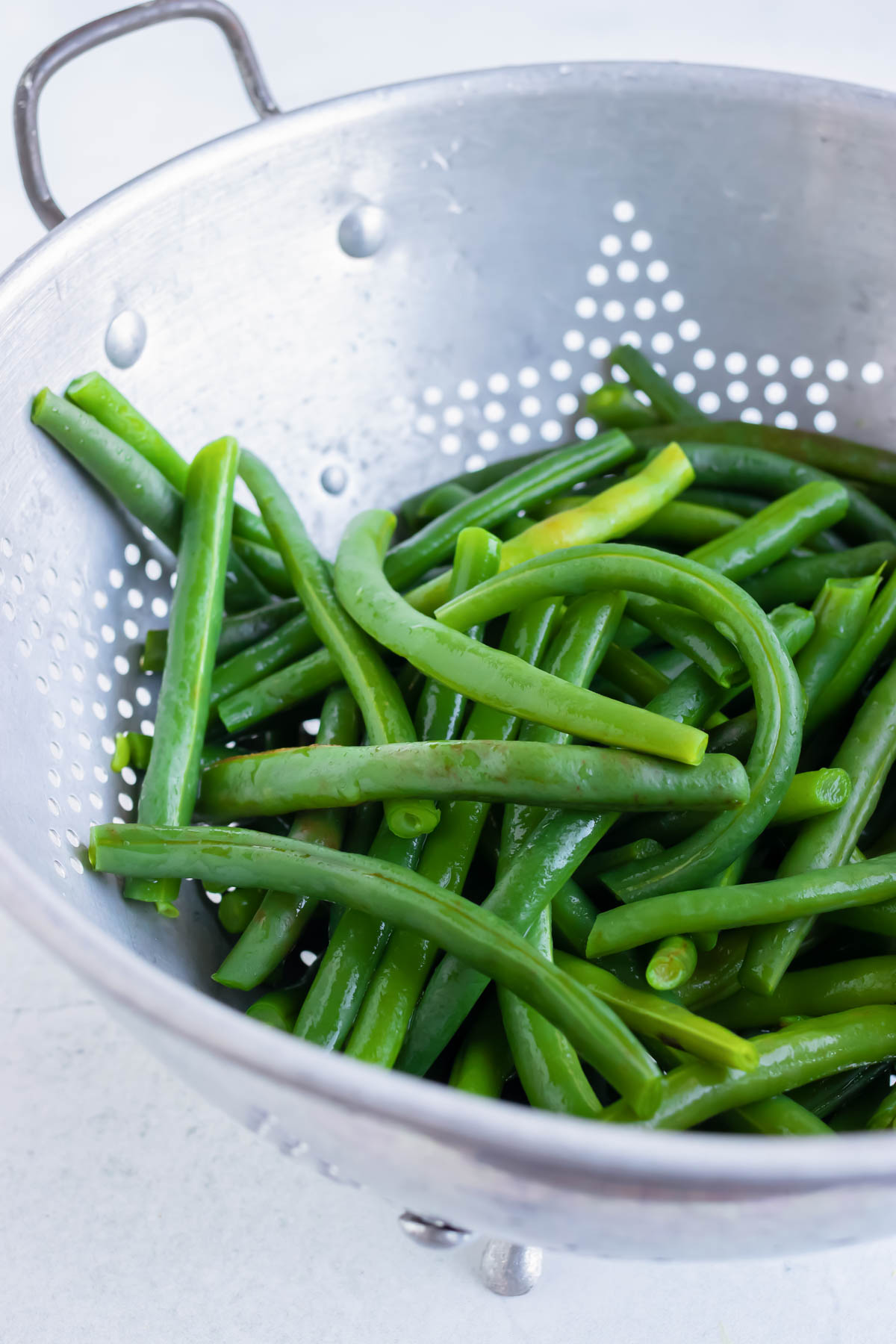 Boiled green beans being drained in a colander.