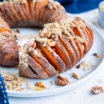 Hasselback sweet potatoes are served on a plate and topped with brown sugar and cinnamon.