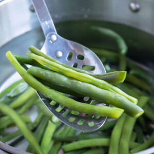 Green beans are removed from a pot of boiling salted water