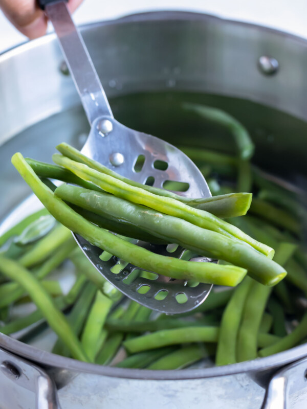 Green beans are removed from a pot of boiling salted water