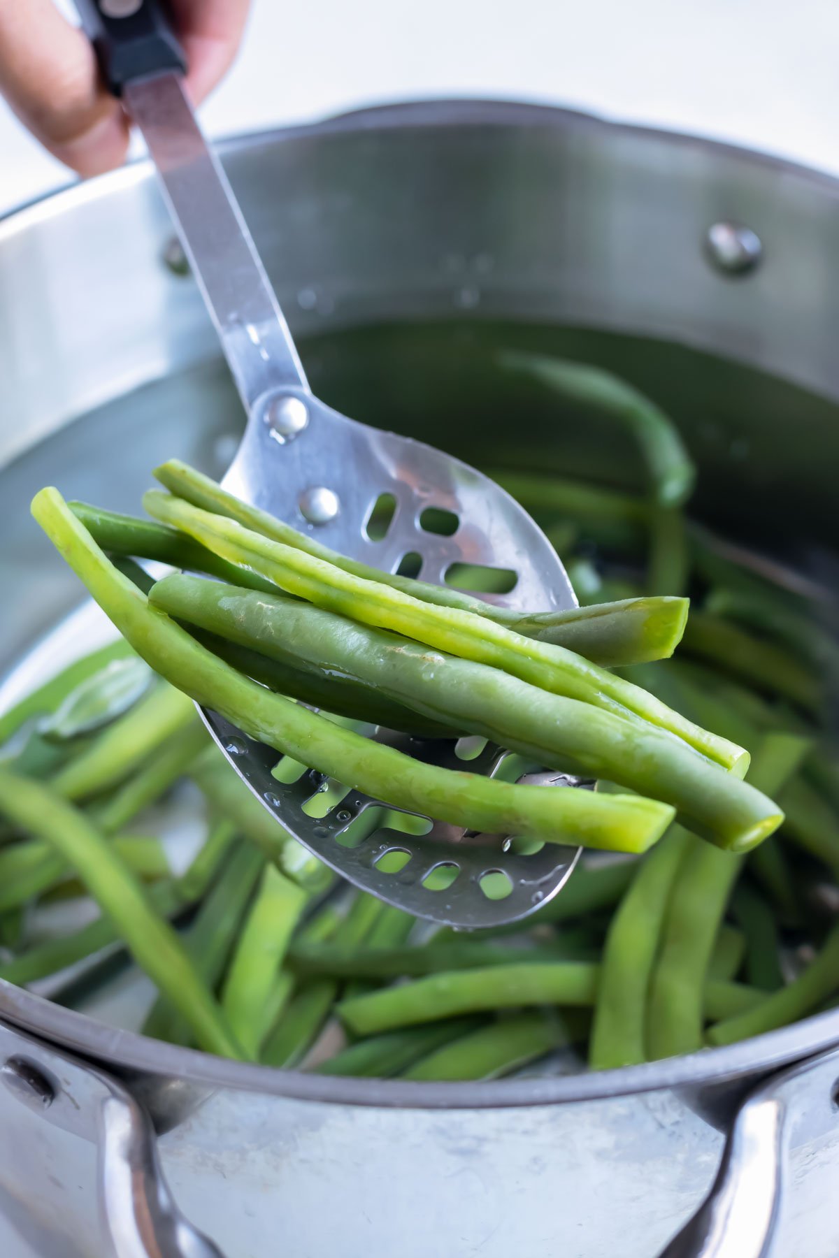 Green beans are removed from the pot by a spoon before blanching.