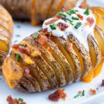 Cheesy hasselback potatoes are topped with sour cream and bacon for a Thanksgiving side.