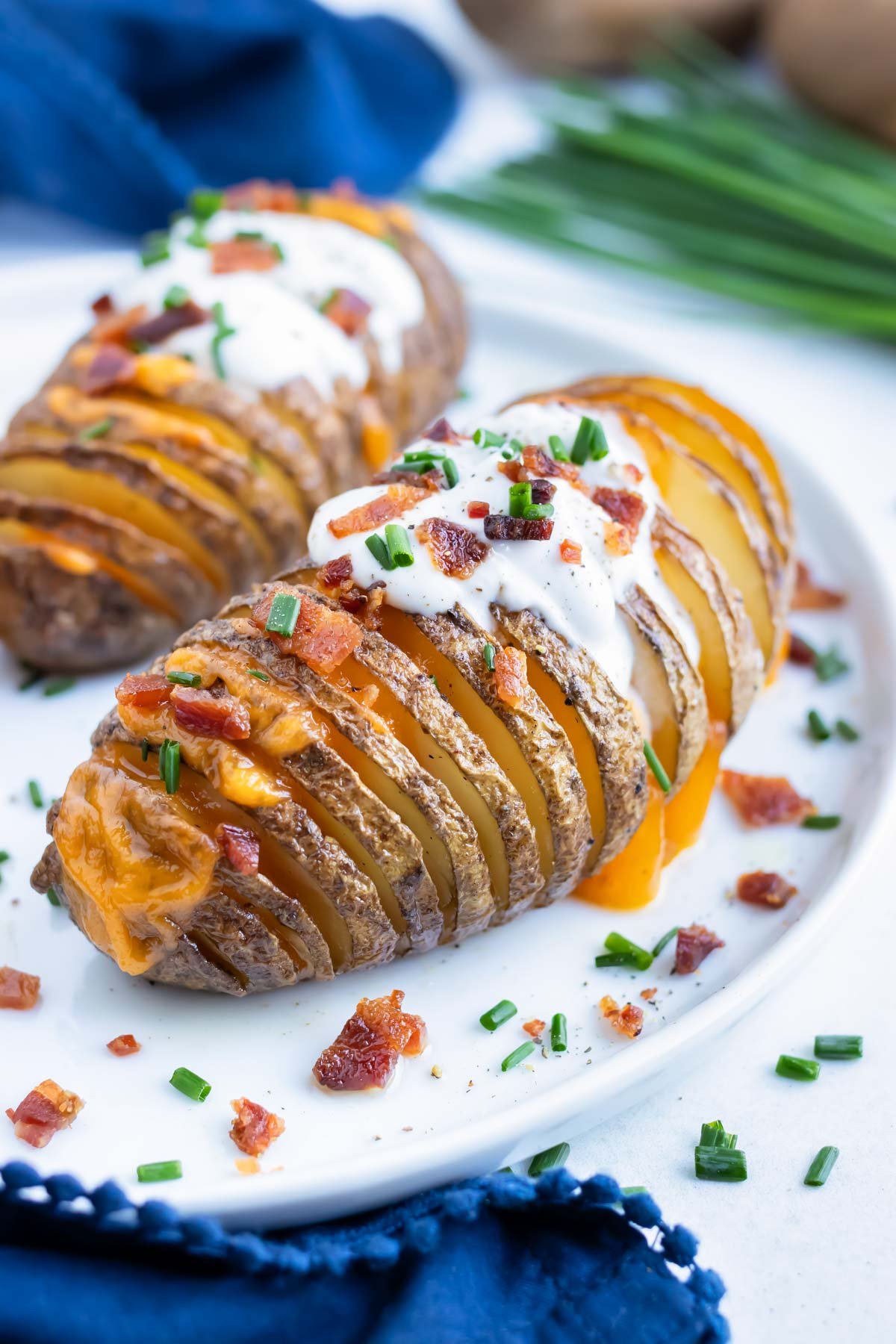 Cheesy Hasselback Potato RECIPE served on a white plate garnished with bacon, sour cream, and chives