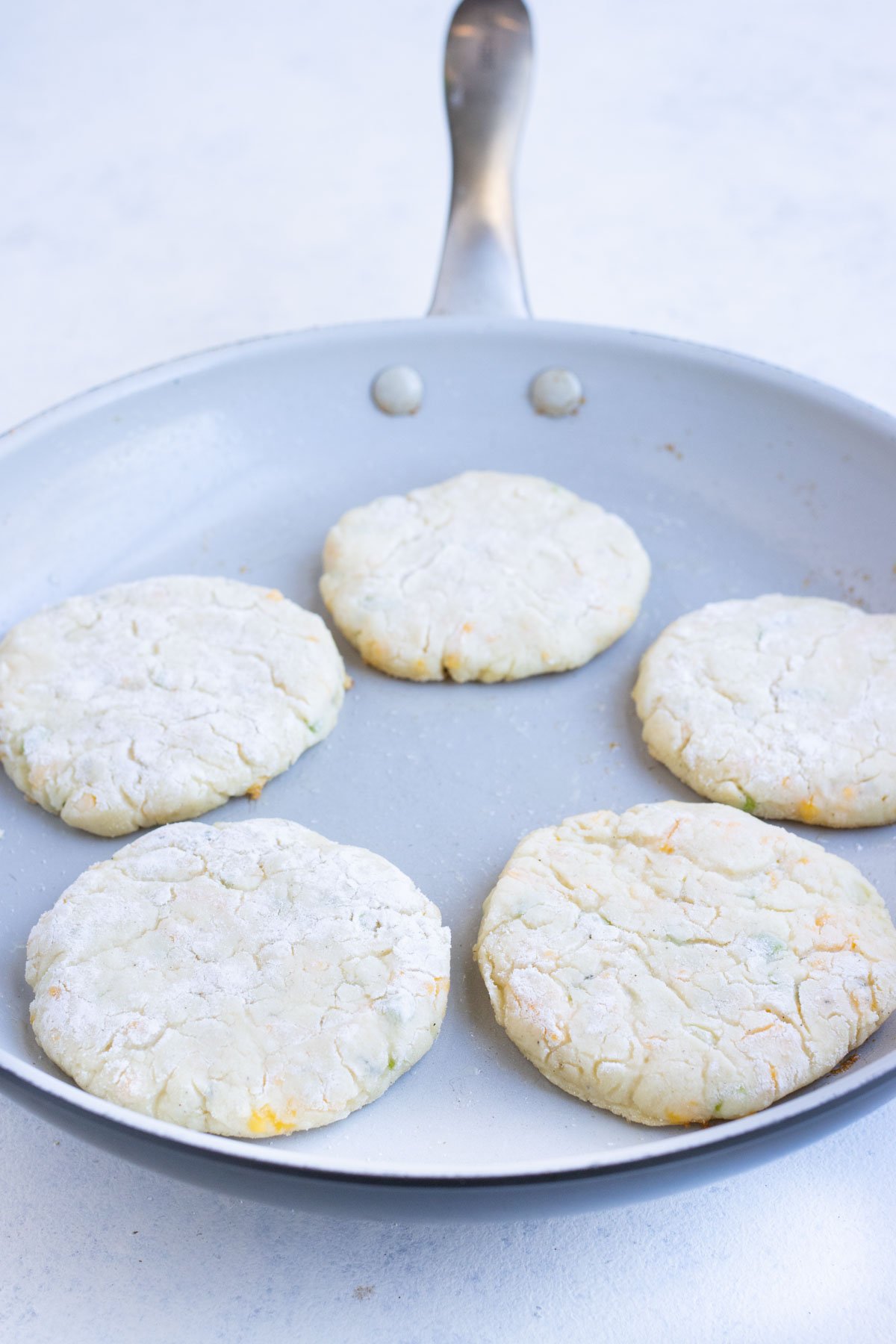 Five pancakes are in a skillet cooking.