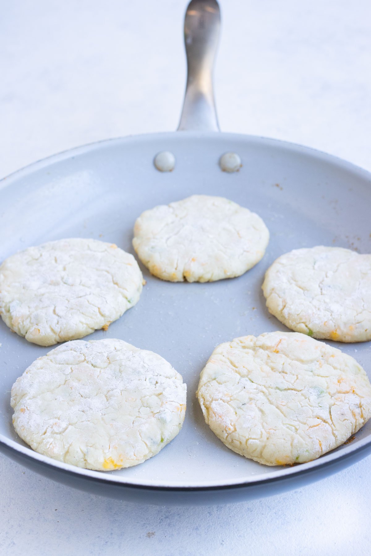 Five pancakes are in a skillet cooking.