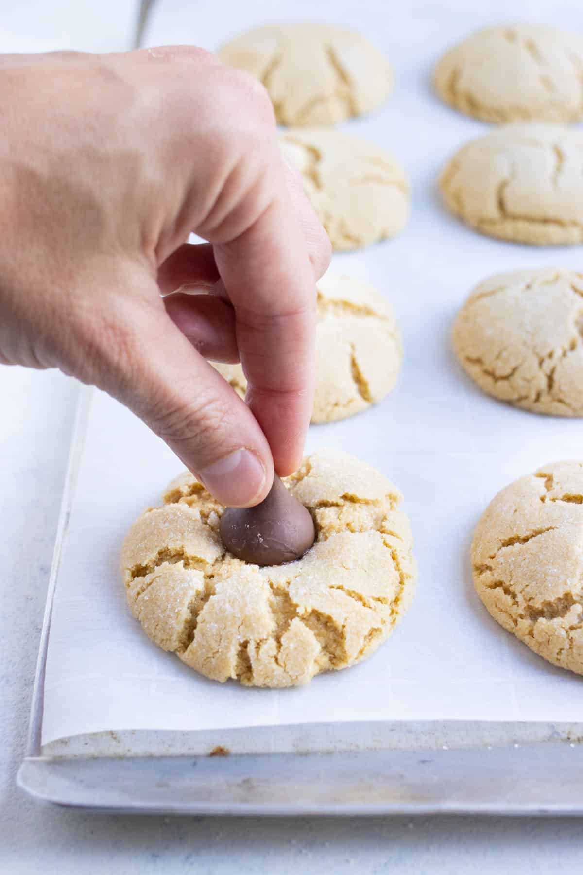 A hand presses in a Hershey's kiss into warm cookies.