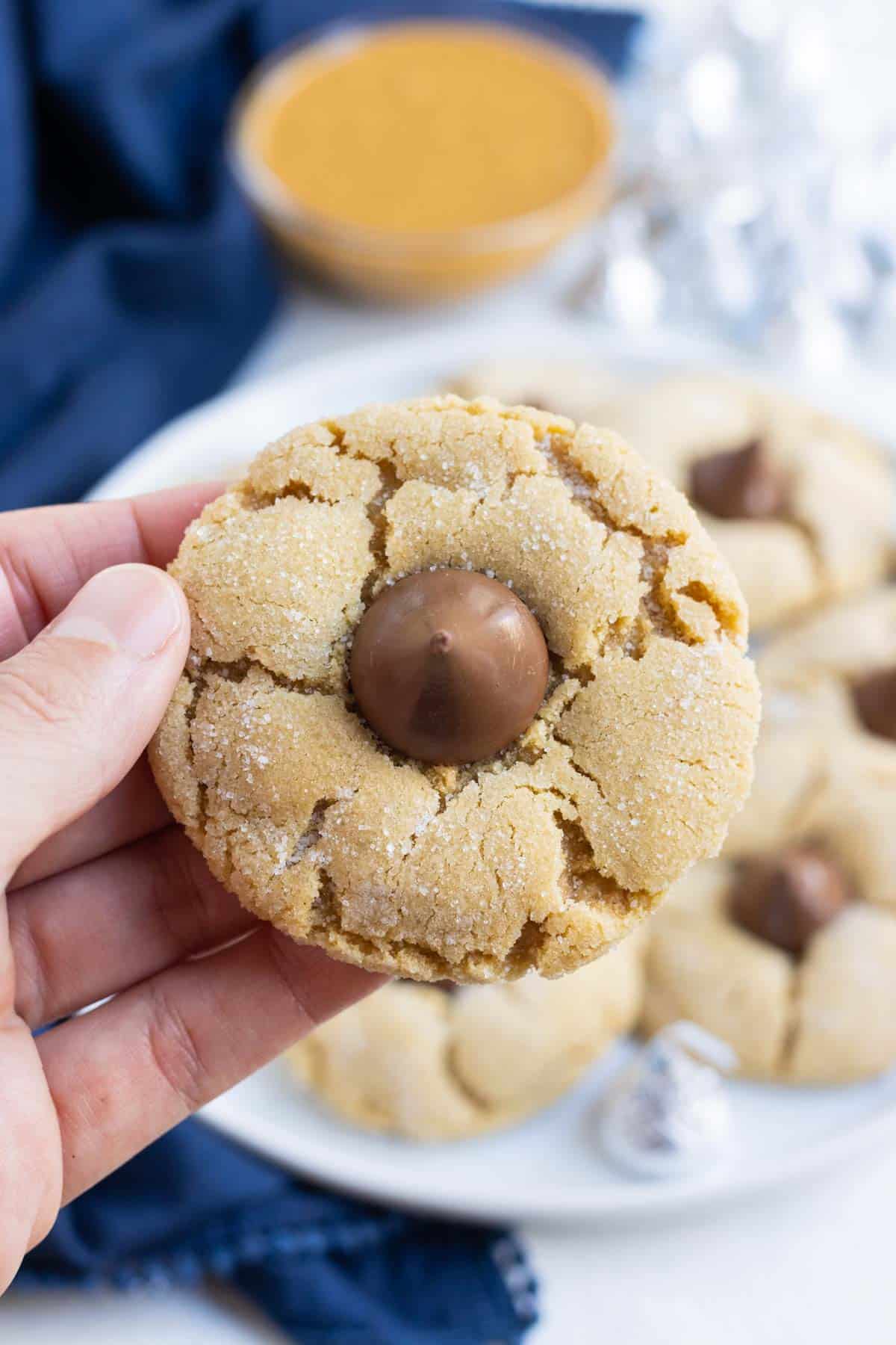 A hand holds a crackly peanut butter blossom cookie.