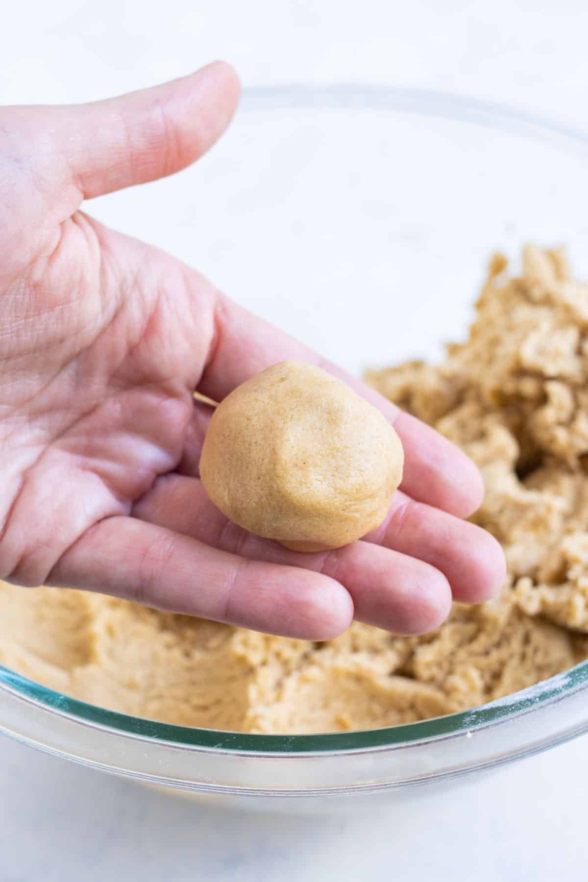 A hand rolls cookie dough into a ball.