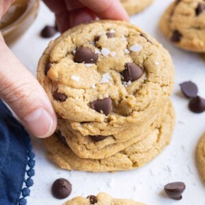 A hand stacks up chocolate chip peanut butter cookies.