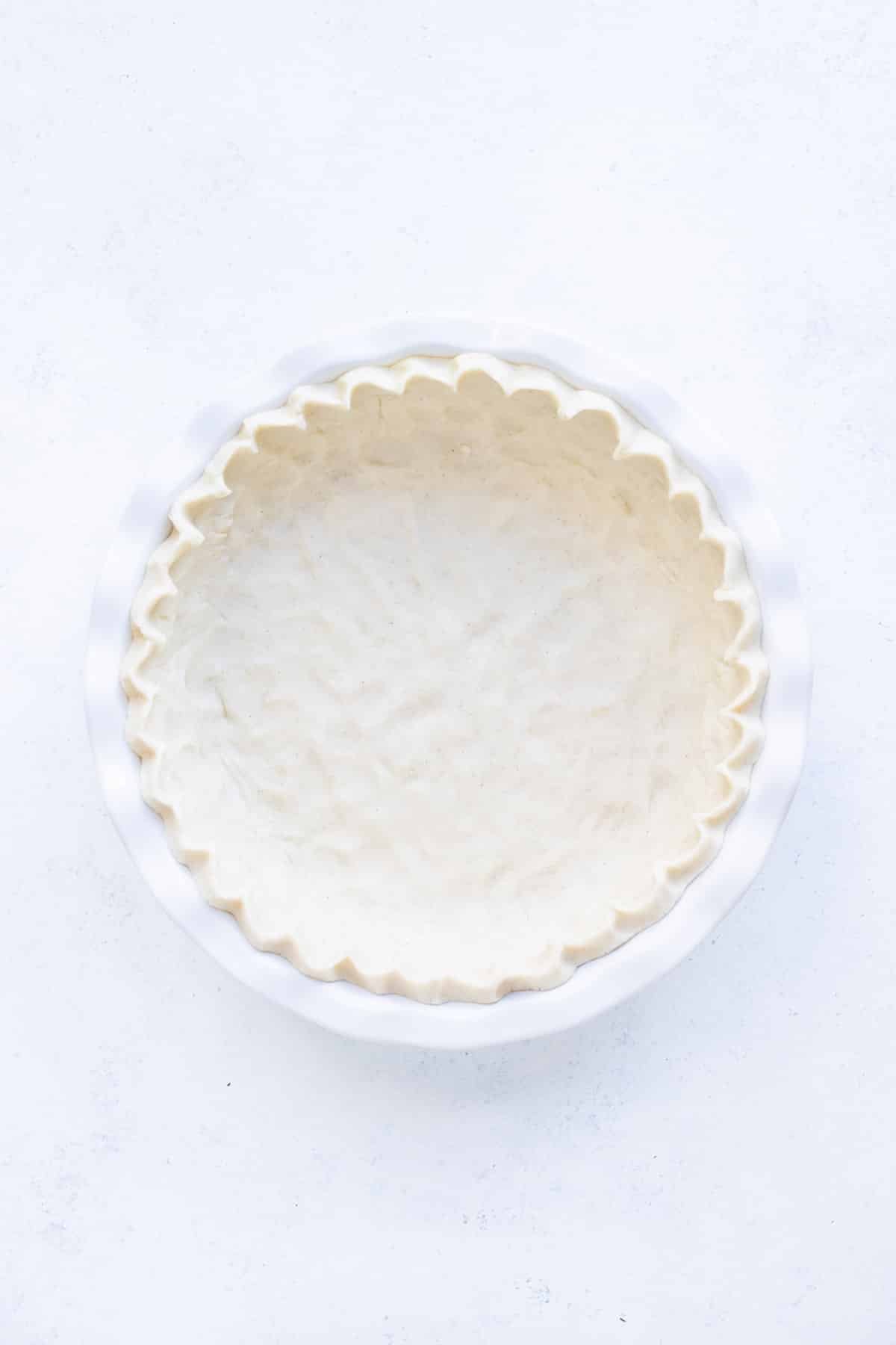 A pie dish has a crust with crimped edges ready to be filled.