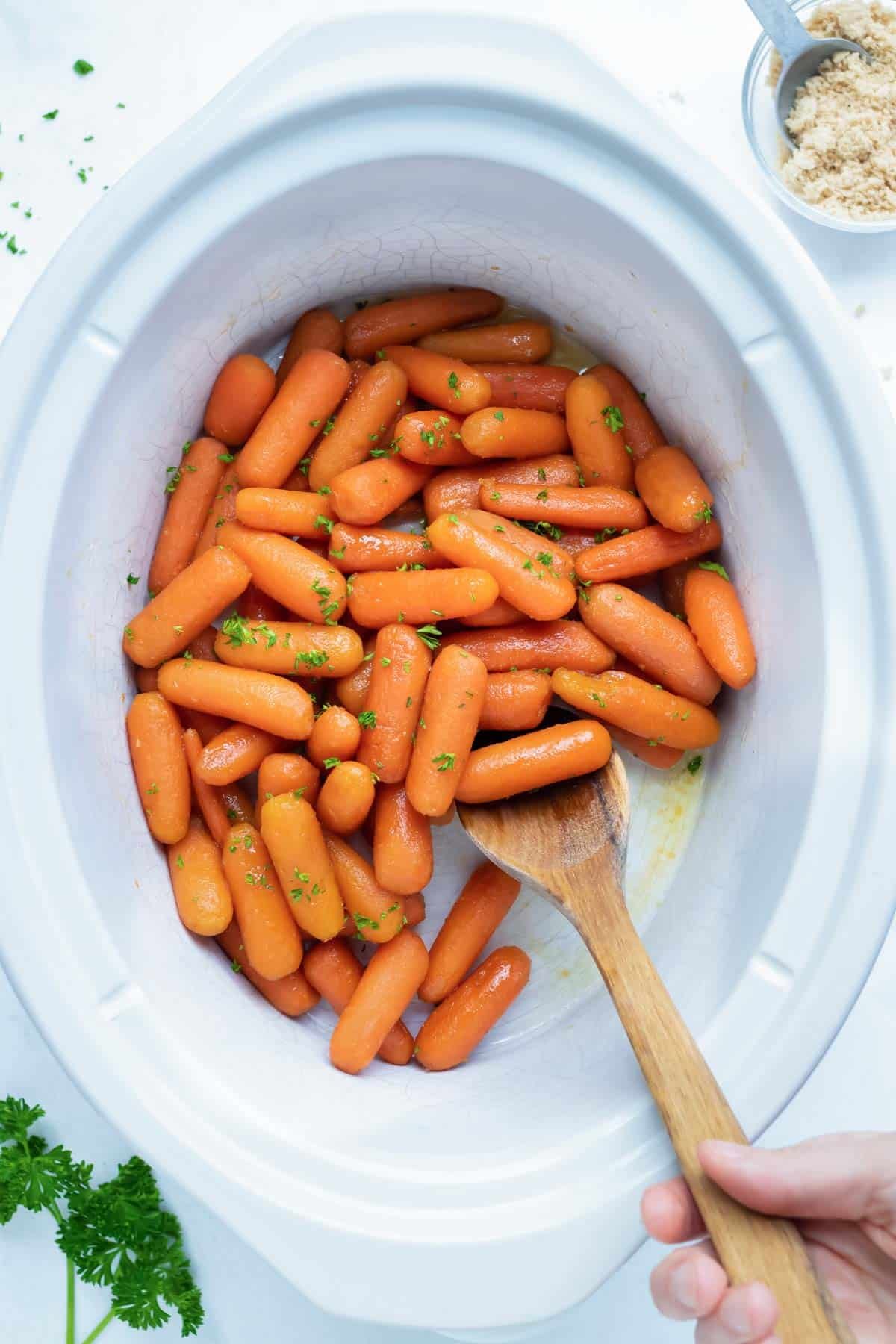 A 6-quart Crock-Pot with baby carrots that have been cooked in a honey, brown sugar, and butter sauce until perfectly glazed.