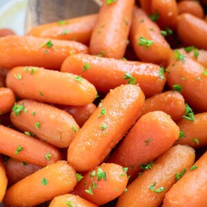 A white slow cooker full of glazed baby carrots with honey and brown sugar.