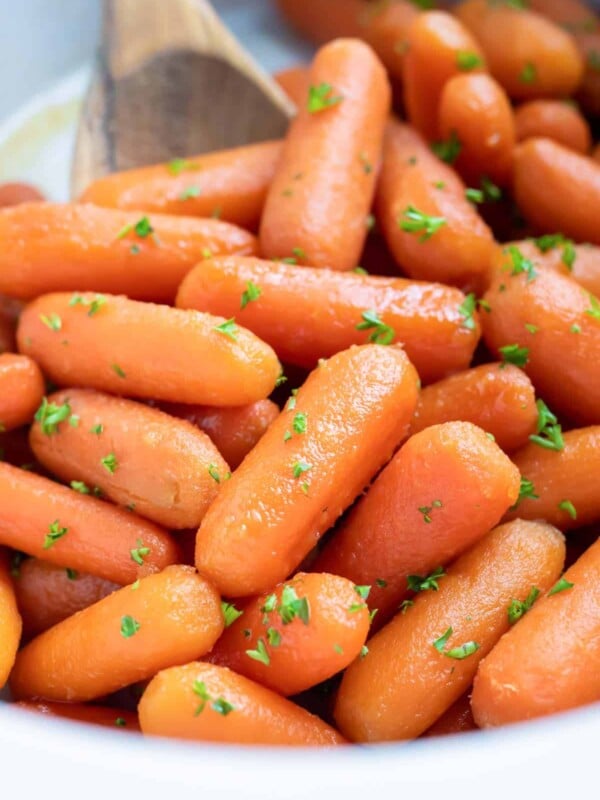 A white slow cooker full of glazed baby carrots with honey and brown sugar.