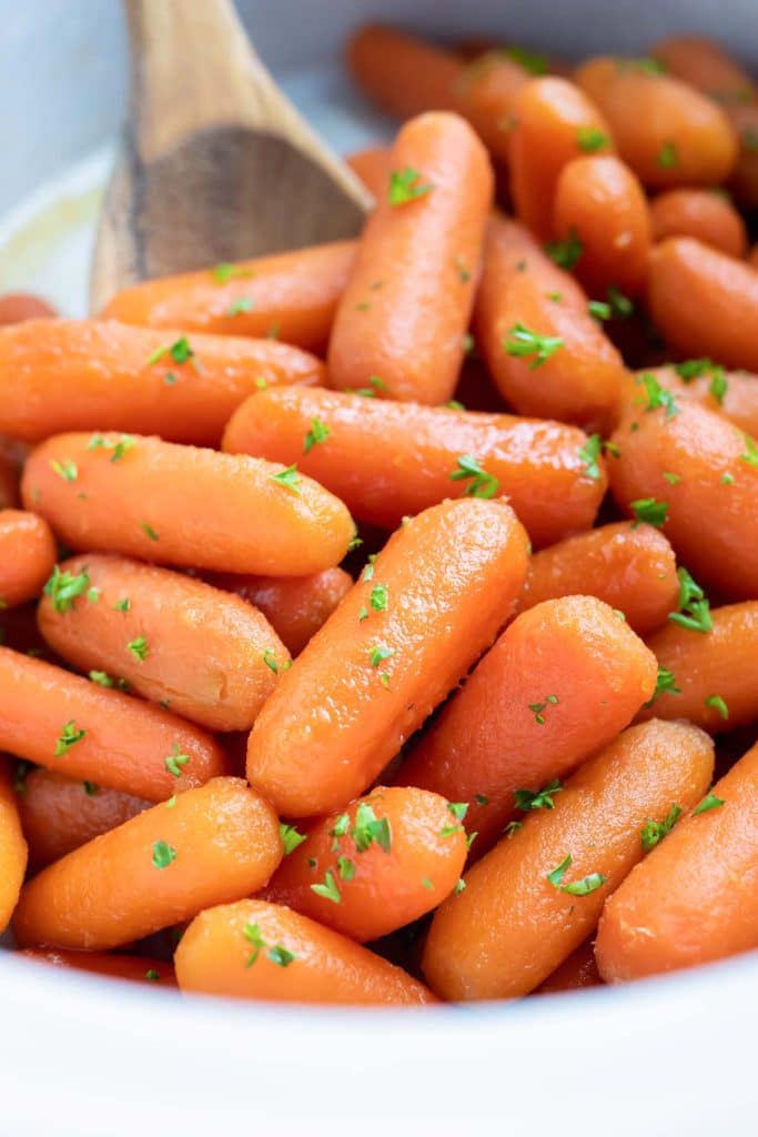 A white slow cooker full of glazed baby carrots with honey and brown sugar.
