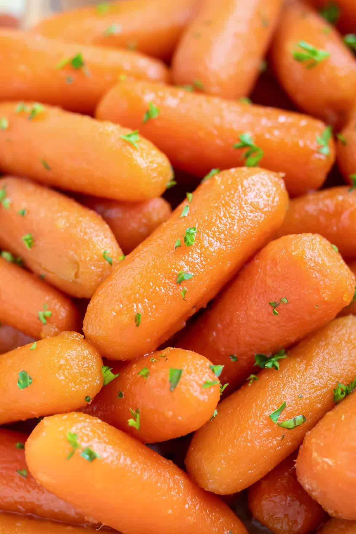 A close-up of baby carrots covered in a honey glaze with parsley sprinkled on top.