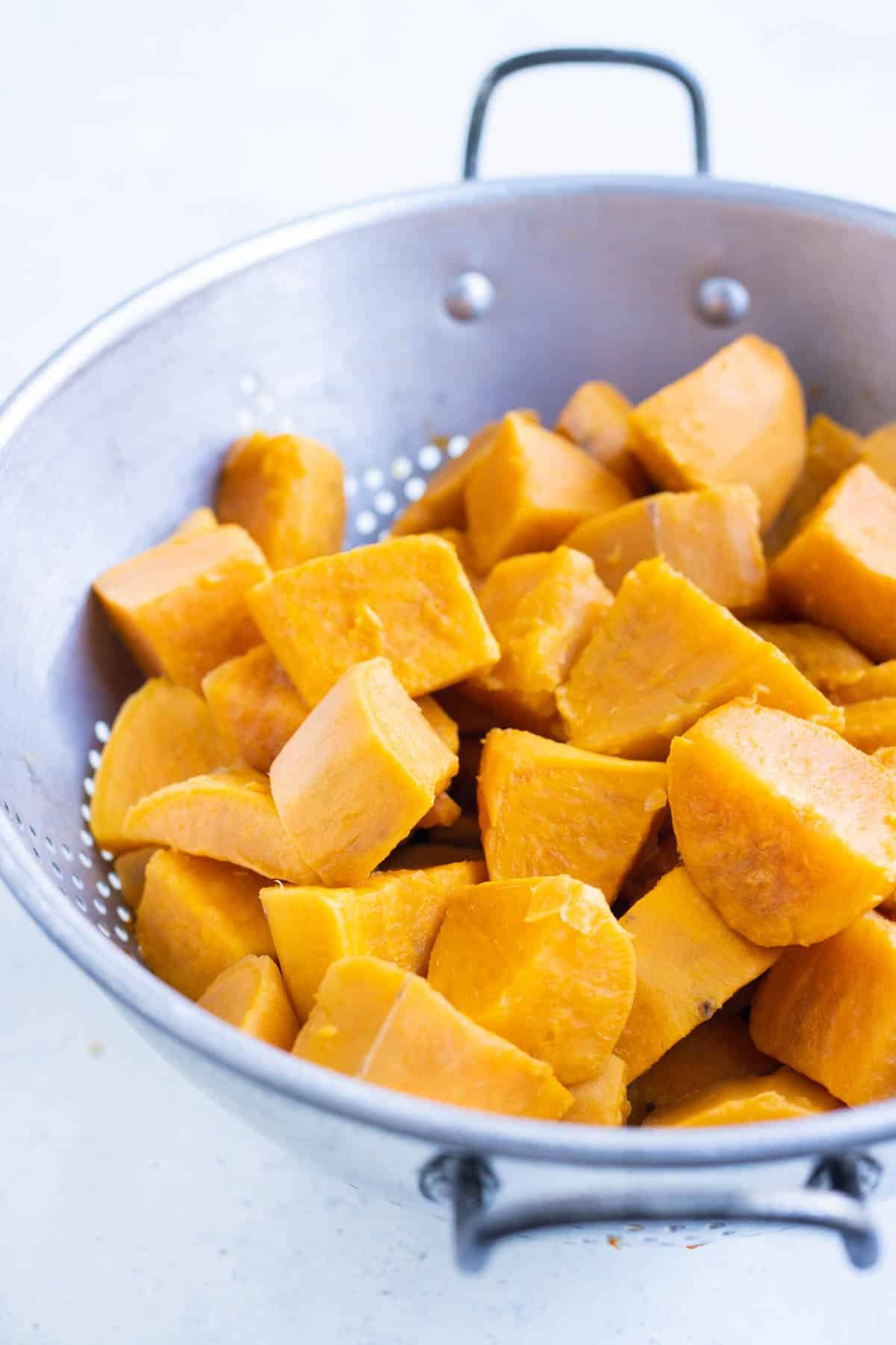 Cubed and diced sweet potatoes are drained in a colander after boiling.