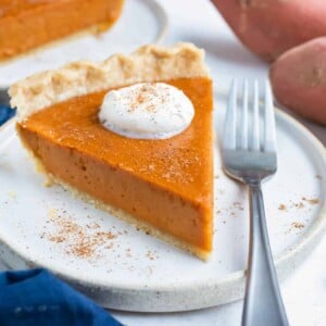 A slice of sweet potato pie is served on a white plate with a fork.