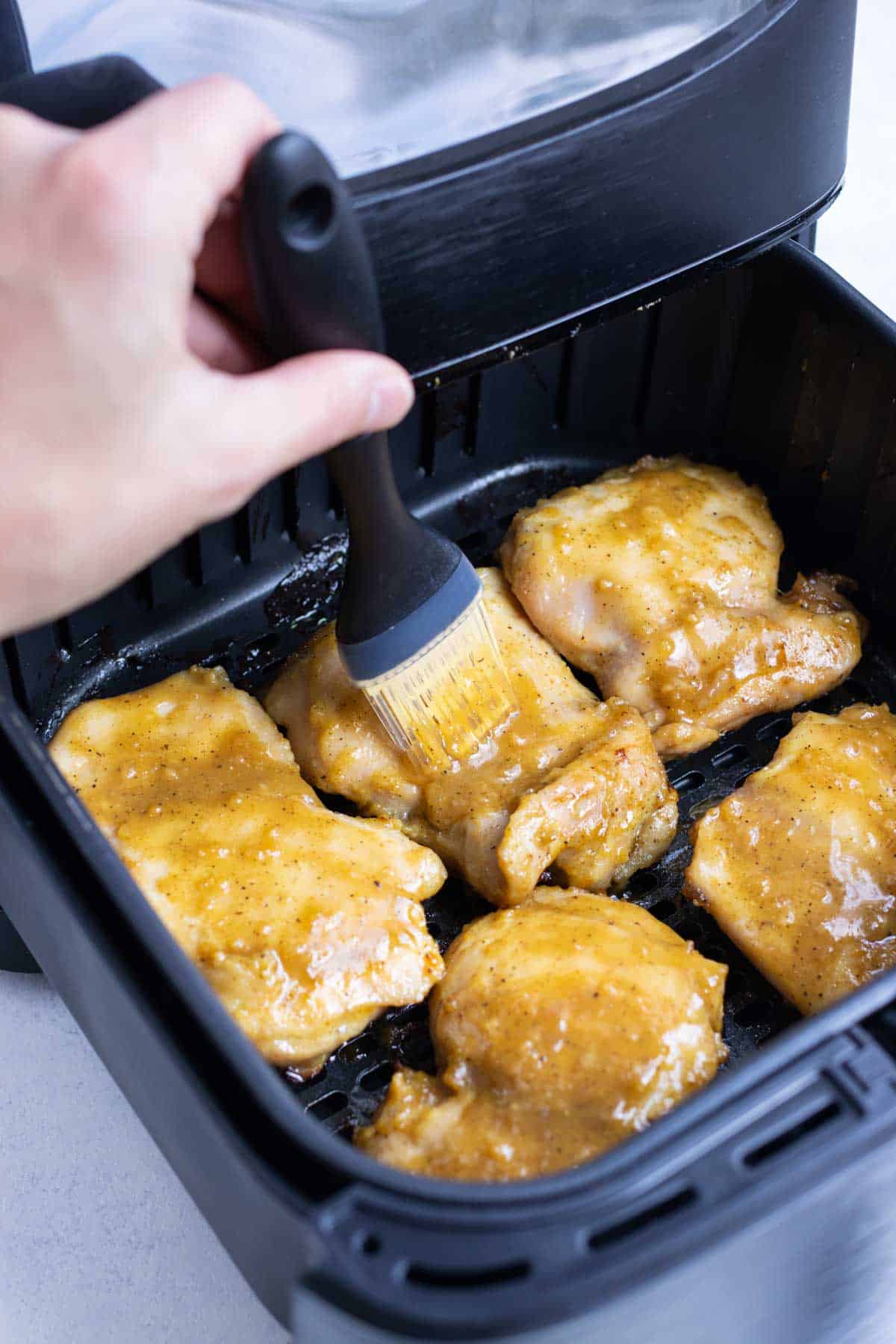 A marinade is brushed onto chicken thighs in an air fryer.