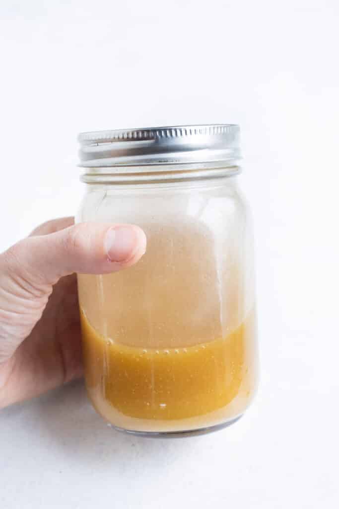 A hand shakes a mason jar with apple cider vinaigrette.