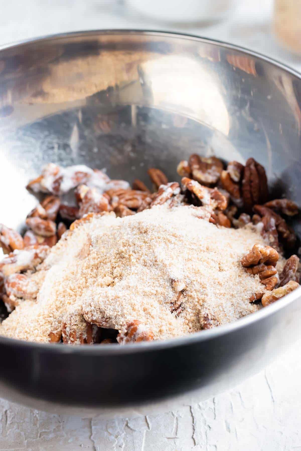 Add cinnamon sugar to a bowl full of pecans.