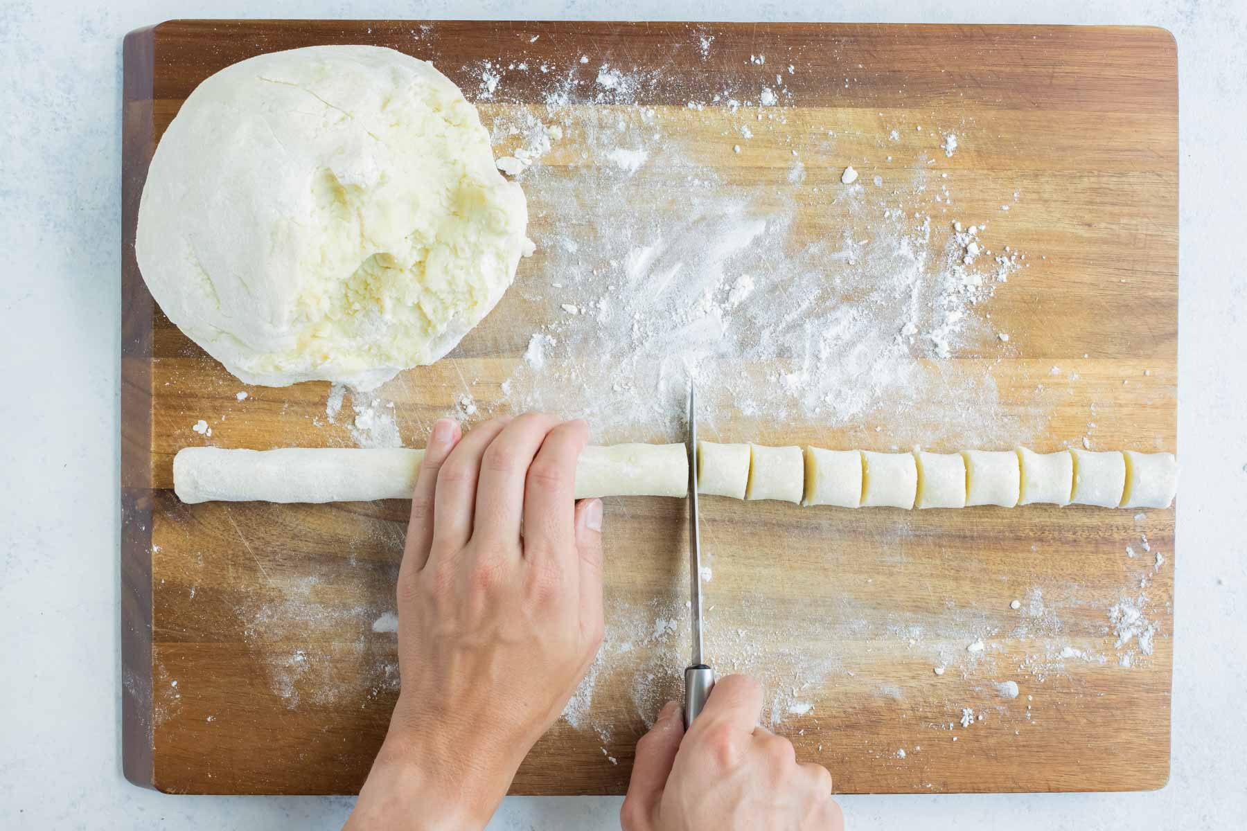 The dough rope is cut into pieces with a knife.