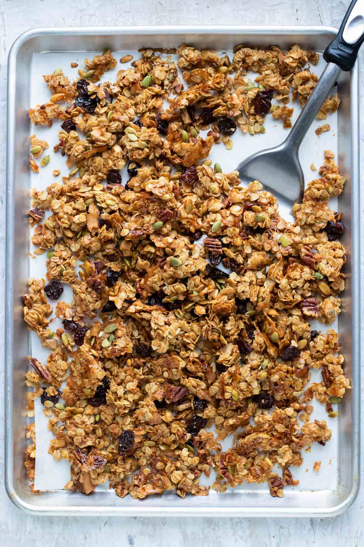 After baking the granola, a spatula breaks the mixture into clusters.