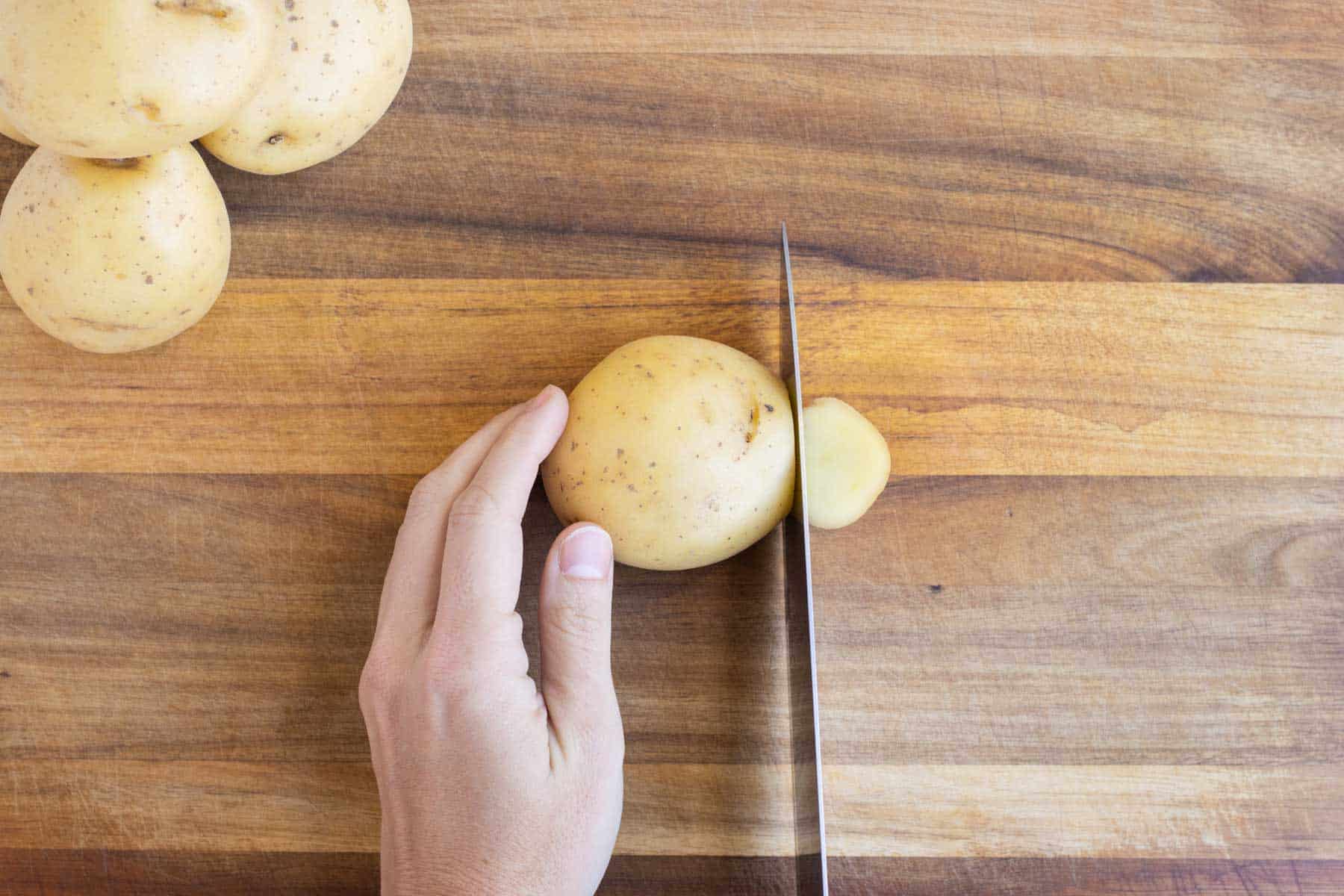 A knife slices the end off of a potato.