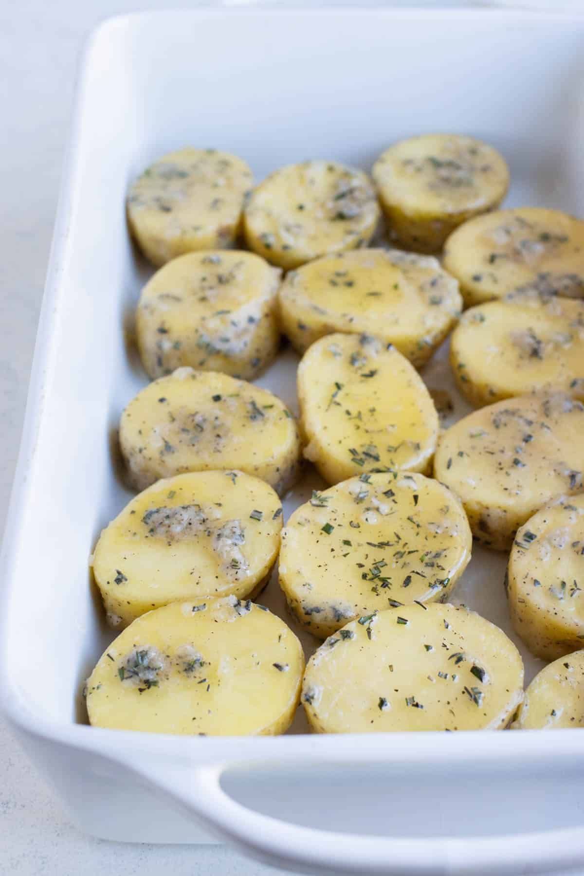 Sauced potatoes are spread in a baking dish.