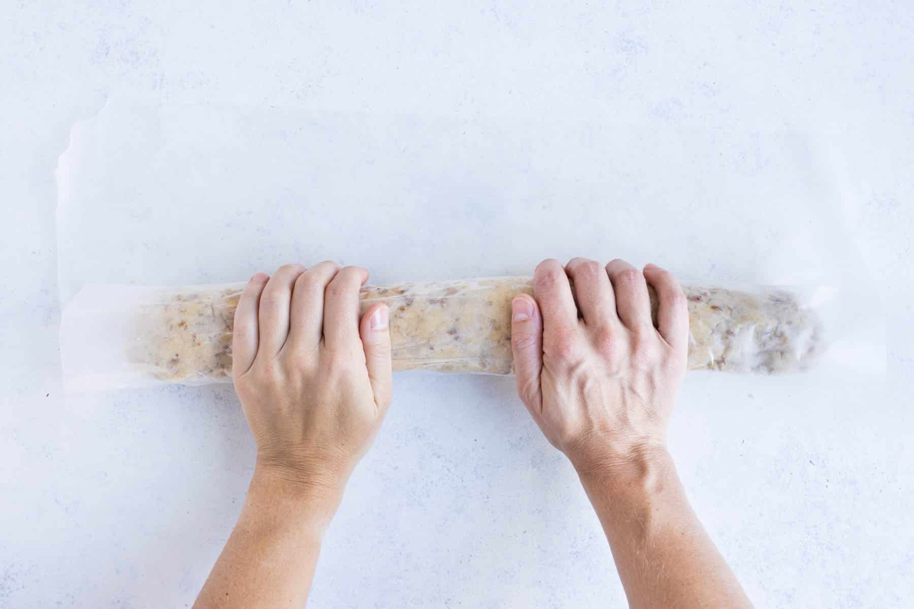 Hands shape cookie dough into a log.