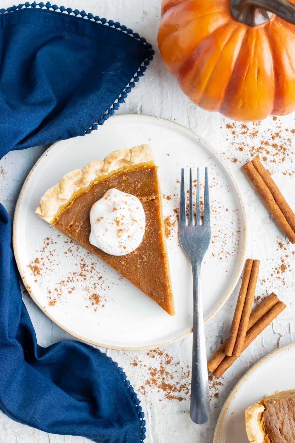 Pumpkin pie slice on a white plate with cinnamon sticks around it before freezing.