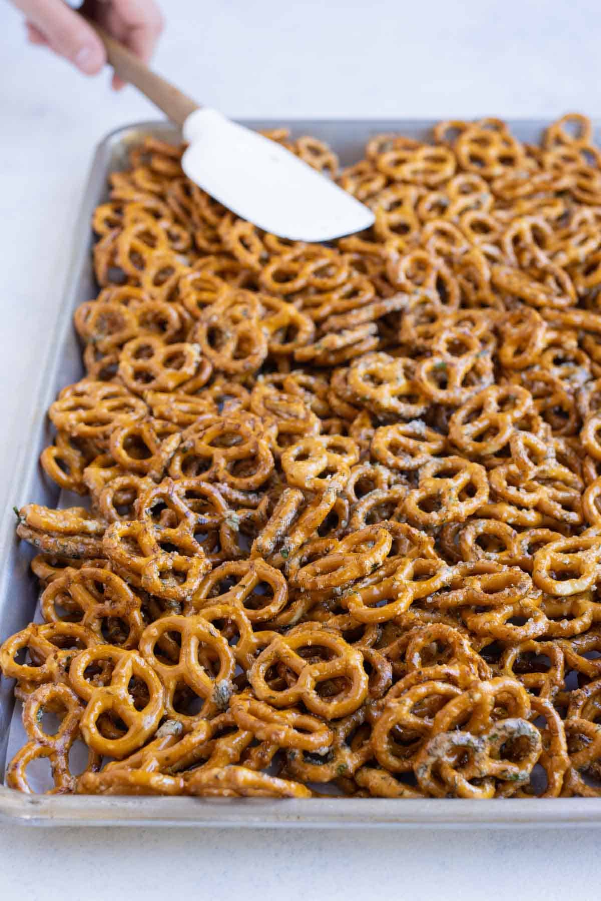 A spatula spreads out seasoned pretzels on a baking sheet.