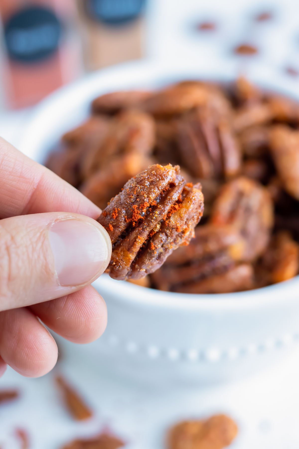 A spiced pecan is held up by a hand for a low-carb snack.