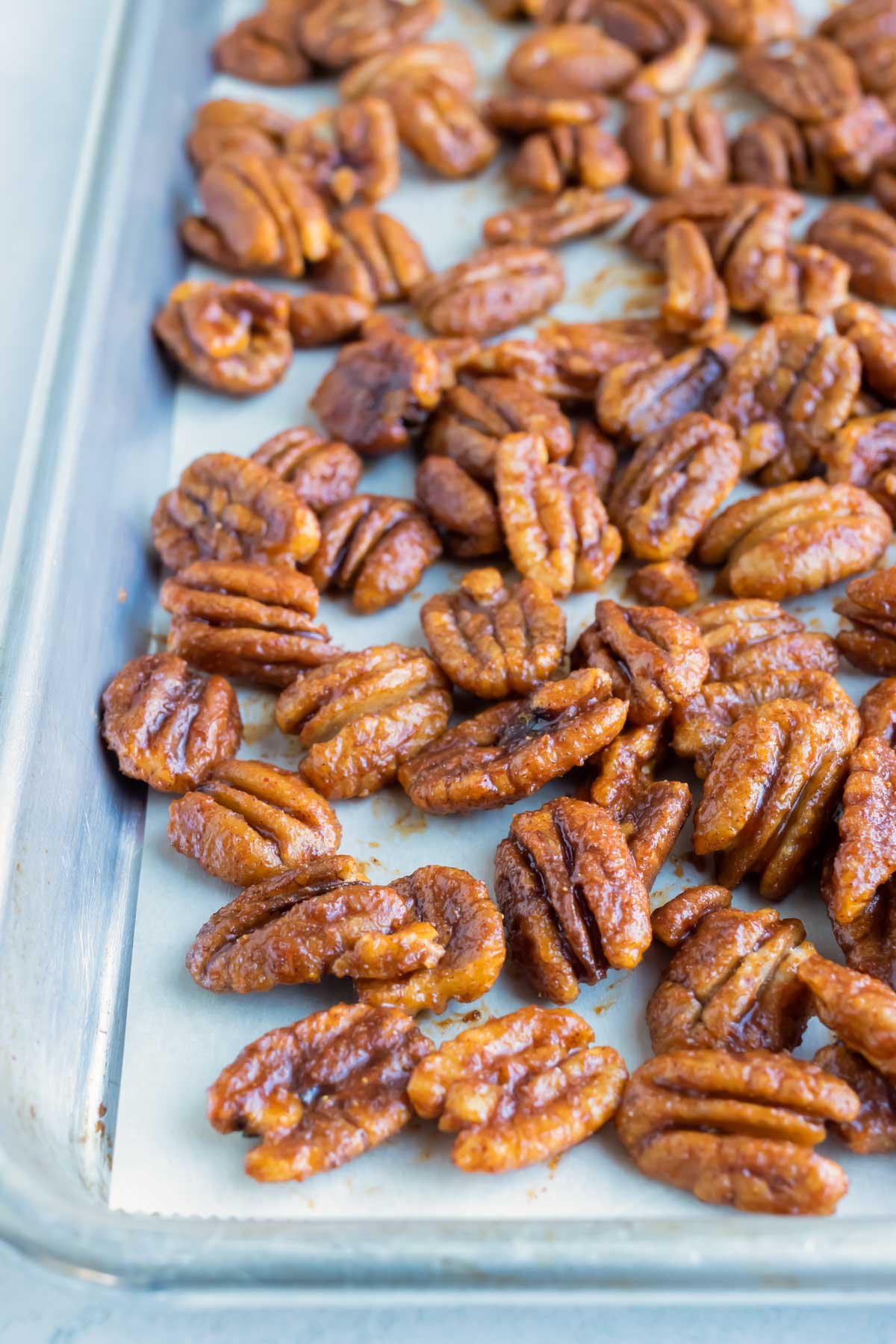 Spicy and sweet coated pecans are laid flat on a large baking sheet.