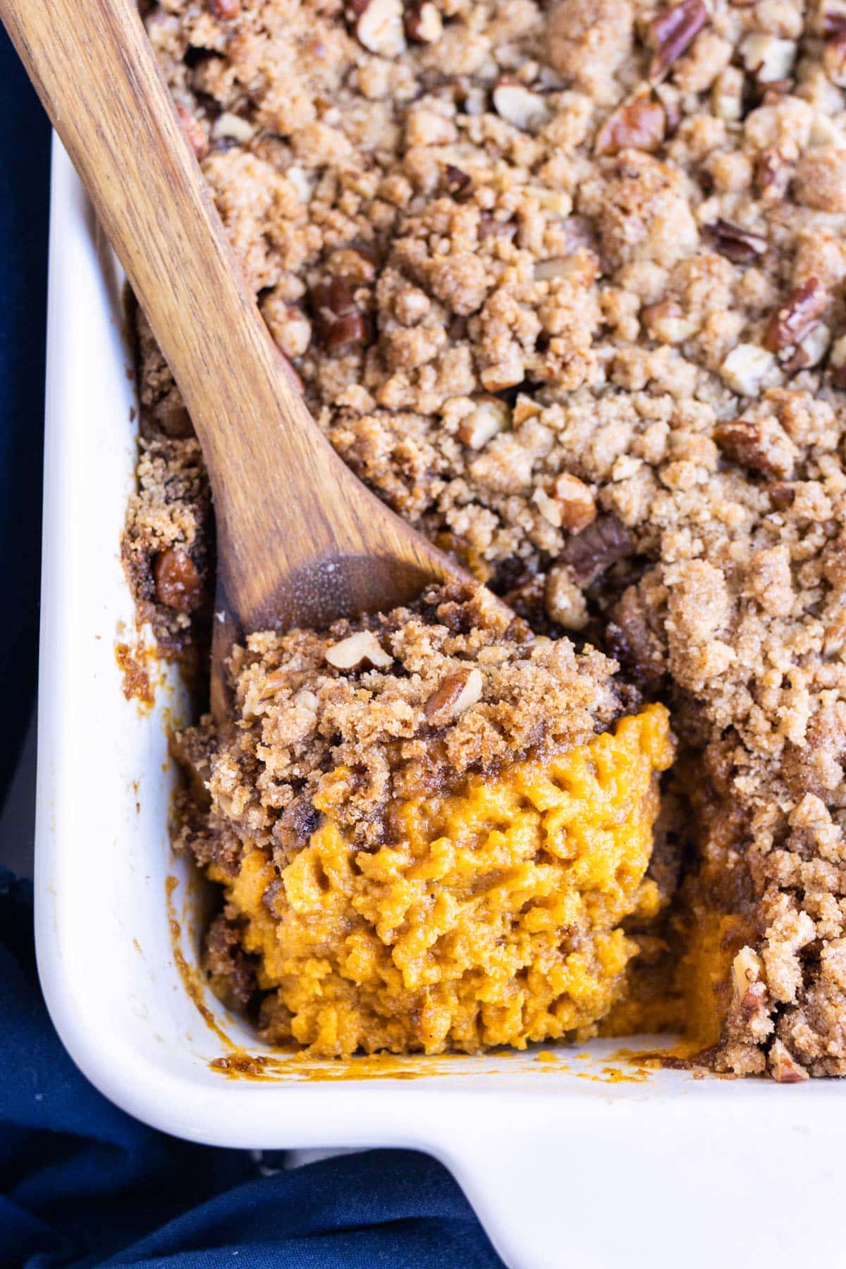 Sweet potato casserole with pecans and brown sugar is served with a spoon for the holidays.