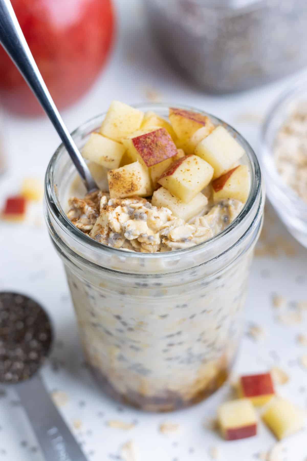 Apple overnight oats made with cinnamon in a glass with a spoon.