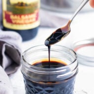 Balsamic glaze being scooped up by a spoon from a clear mason jar container.