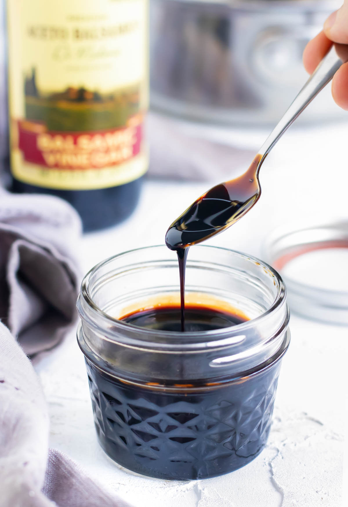 Balsamic glaze being scooped up by a spoon from a clear mason jar container.