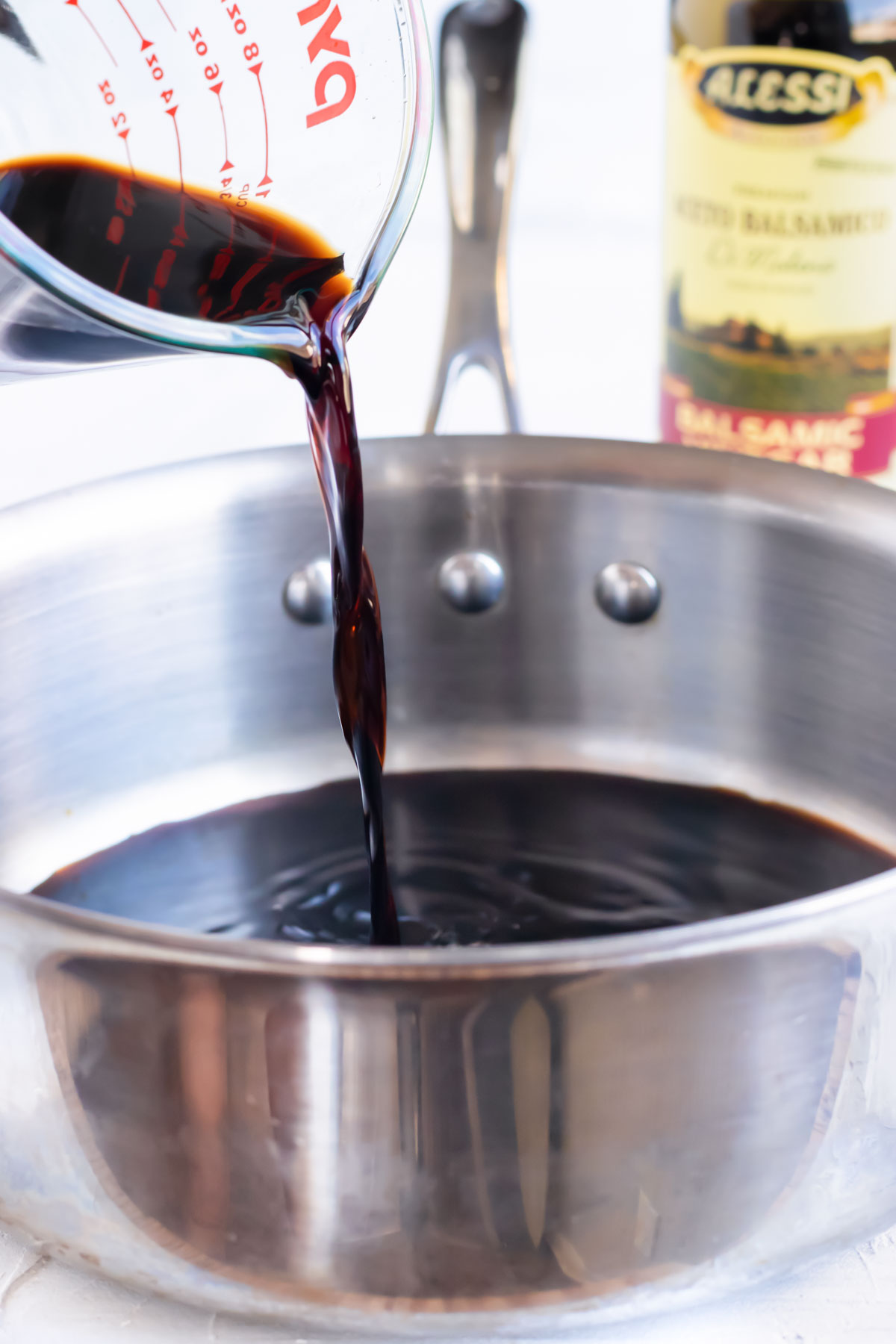 Balsamic vinegar of Modena being poured into a stainless steel saucepan for a balsamic reduction recipe.