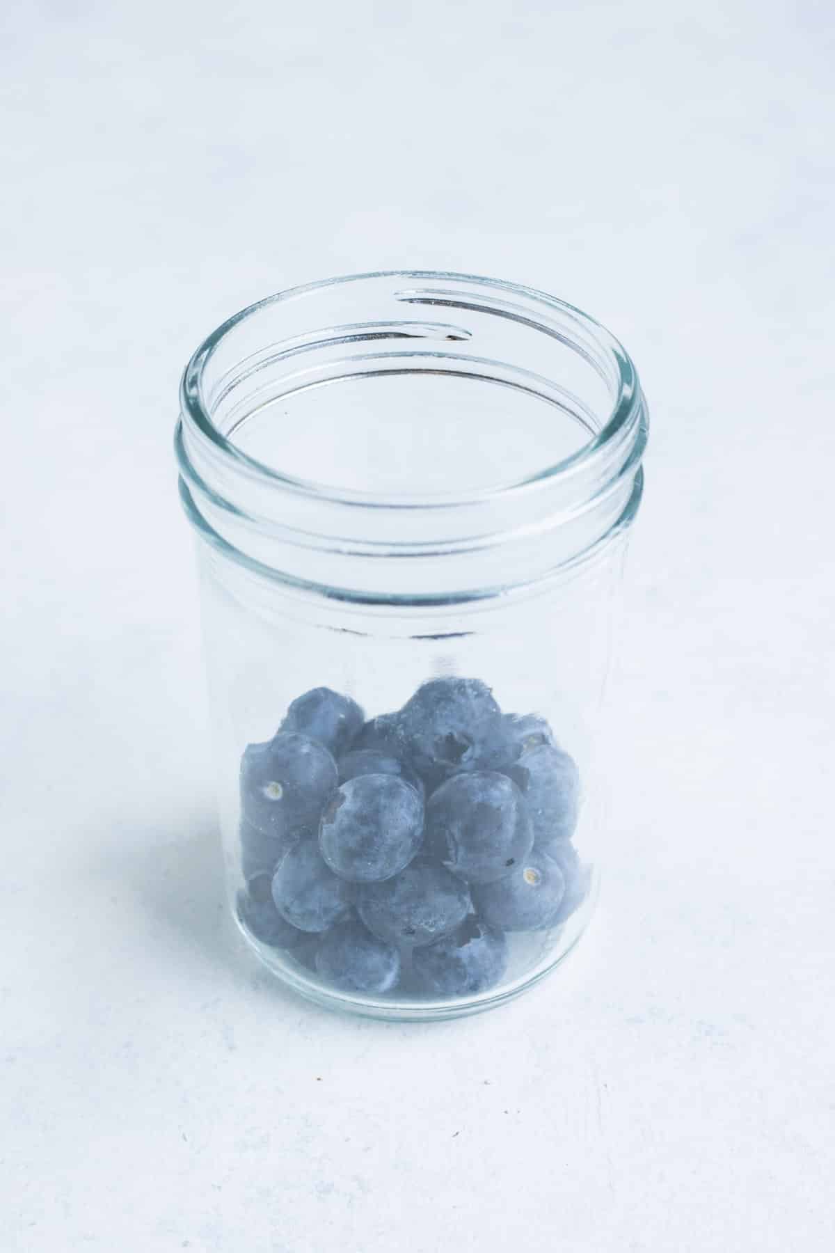 Blueberries are added to a mason jar.