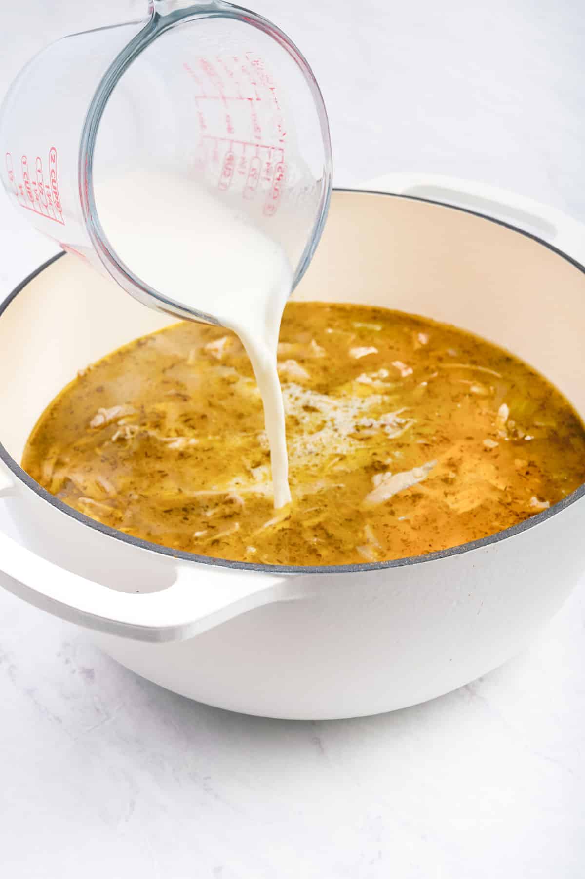 A starch slurry being poured into a pot full of gnocchi soup with chicken.