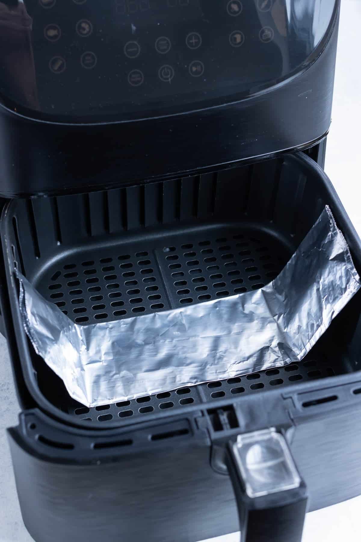 Tin foil folded upwards like handles in an air fryer basket.