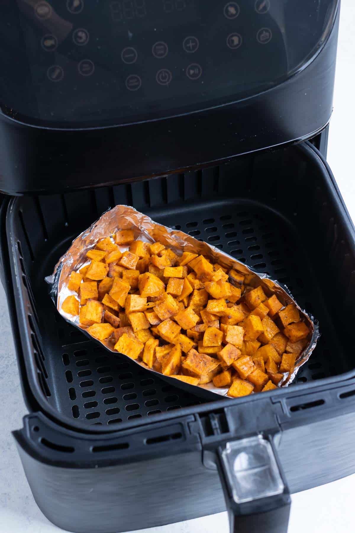 A basket of aluminum foil holding sweet potatoes in an air fryer.