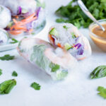 Two spring rolls are set on the counter with a homemade peanut sauce.