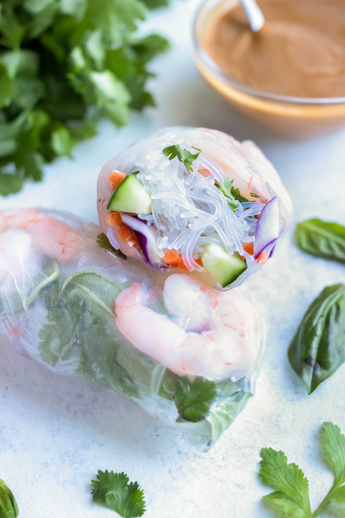 Fresh spring rolls are shown on the counter with herbs and a peanut sauce behind them.