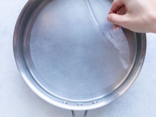 A hand pulls a piece of rice paper out of the water.