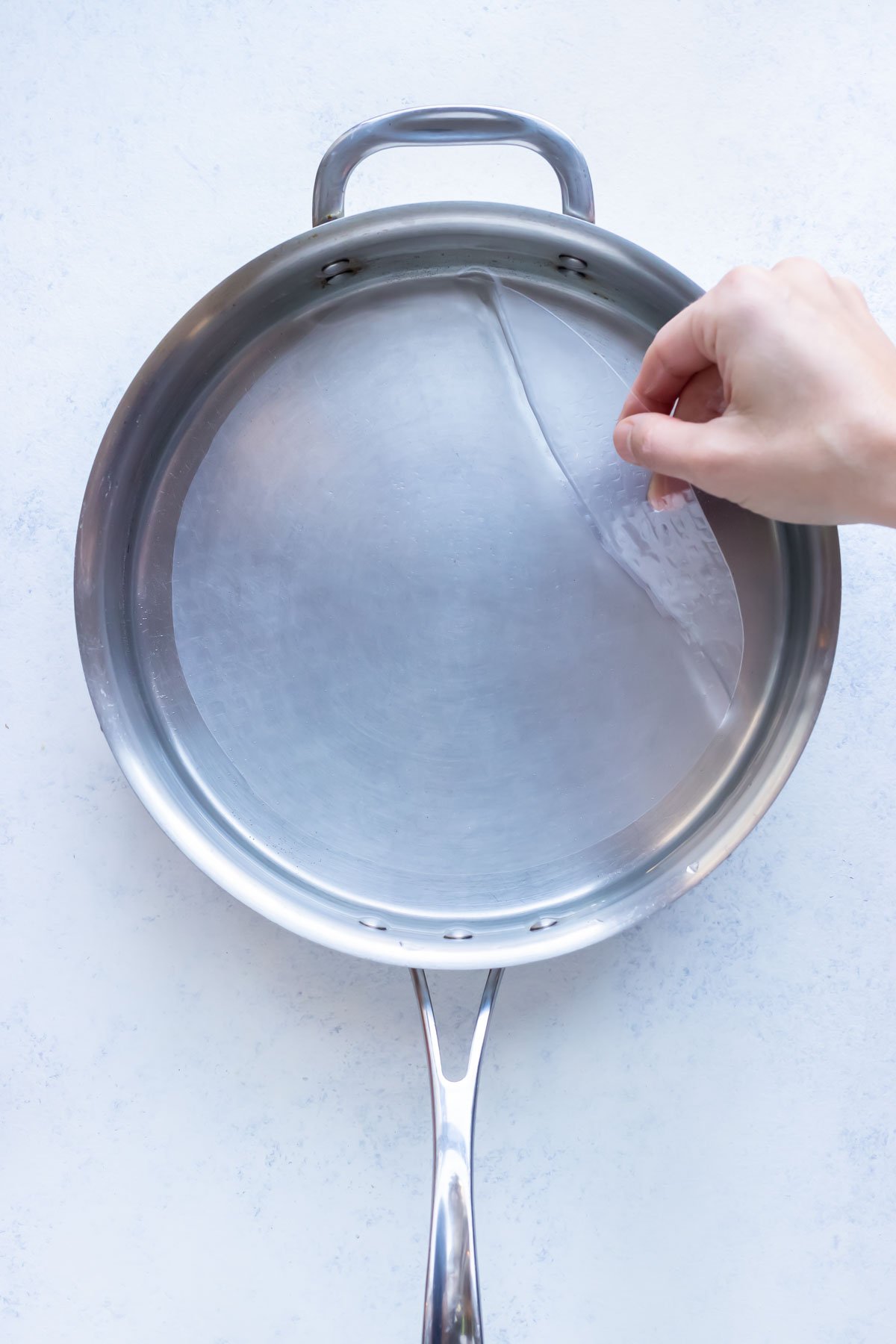 A hand pulls a piece of rice paper out of the water.